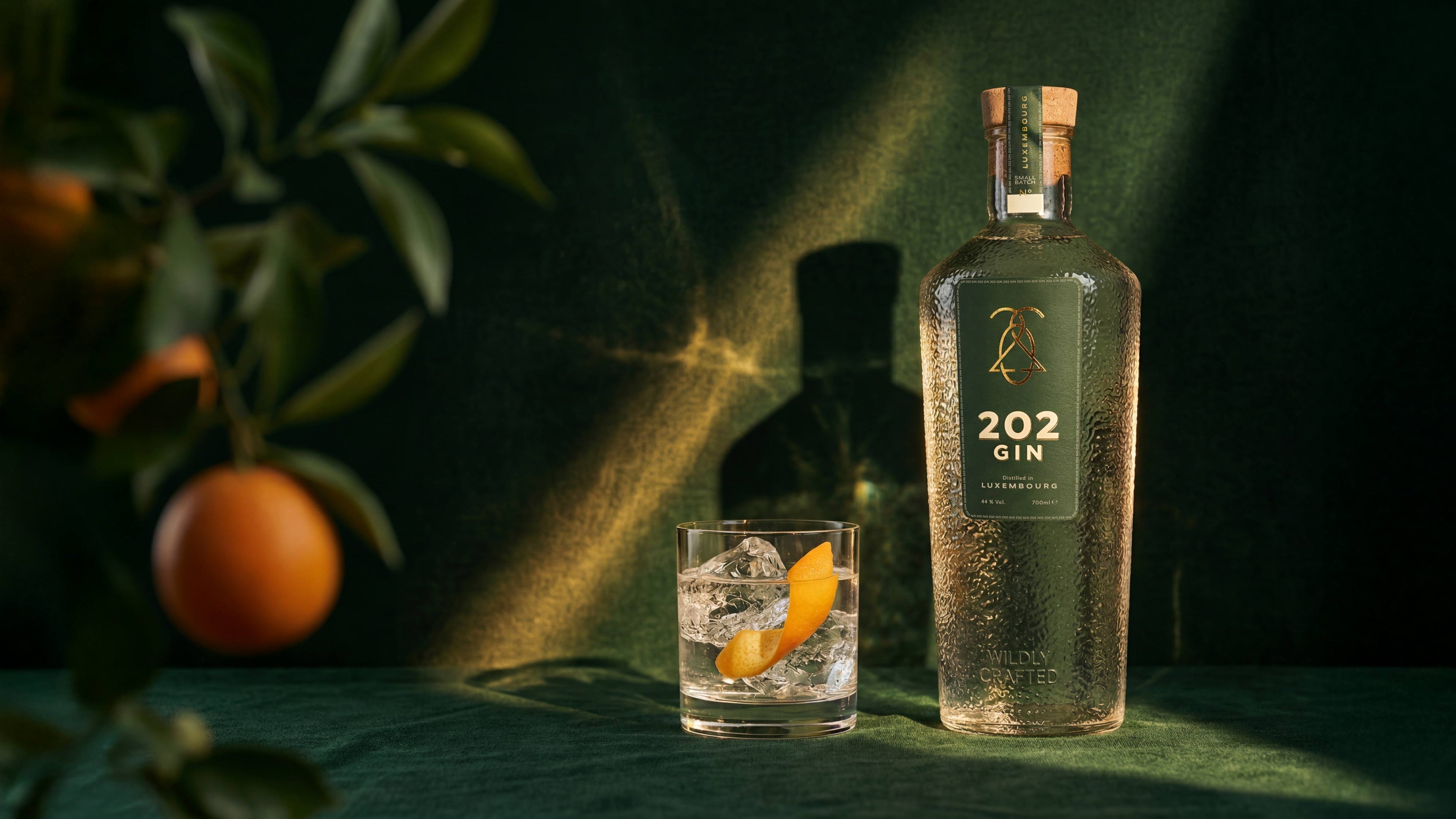 202 GIN distilled in Luxembourg bottle and gin glass with ice presented with an orange tree branch